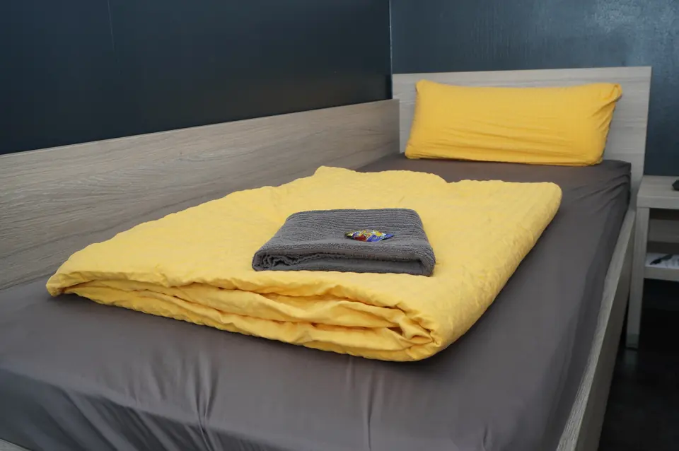 Einzelzimmer mit Bett, gelber Bettwäsche und Handtuch